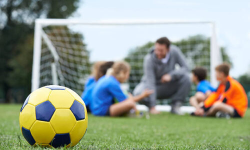Coach  And Team Discussing Soccer Tactics With Ball In Foreground
